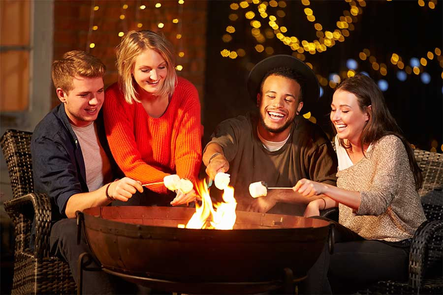 Friends toasting marshmallows over a fire pit in a garden 