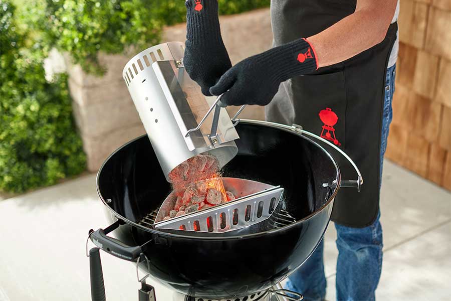 Man lighting a Weber Kettle charcoal barbecue with the Rapidfire Chimney Starter