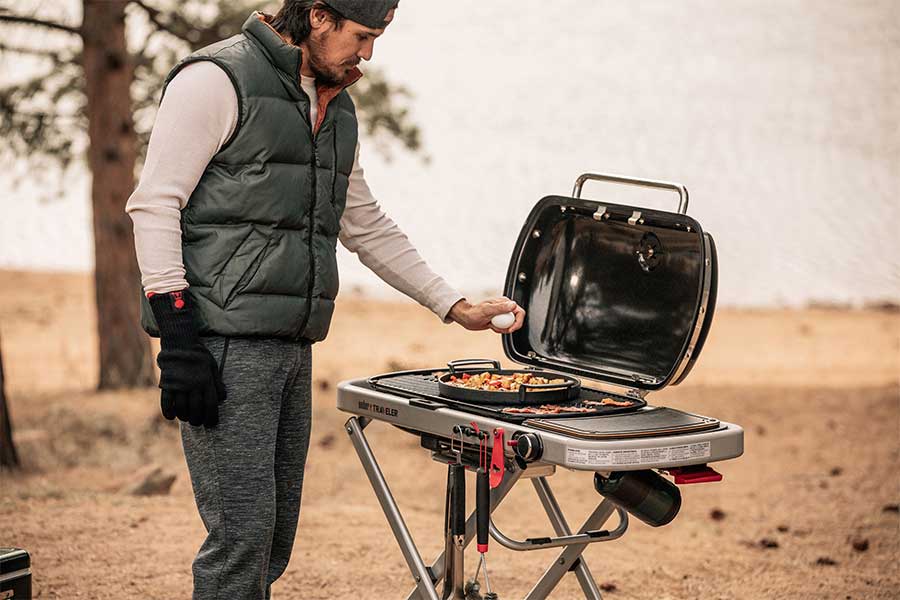 Man using a Weber Traveler portable gas barbecue on a day out in the forest