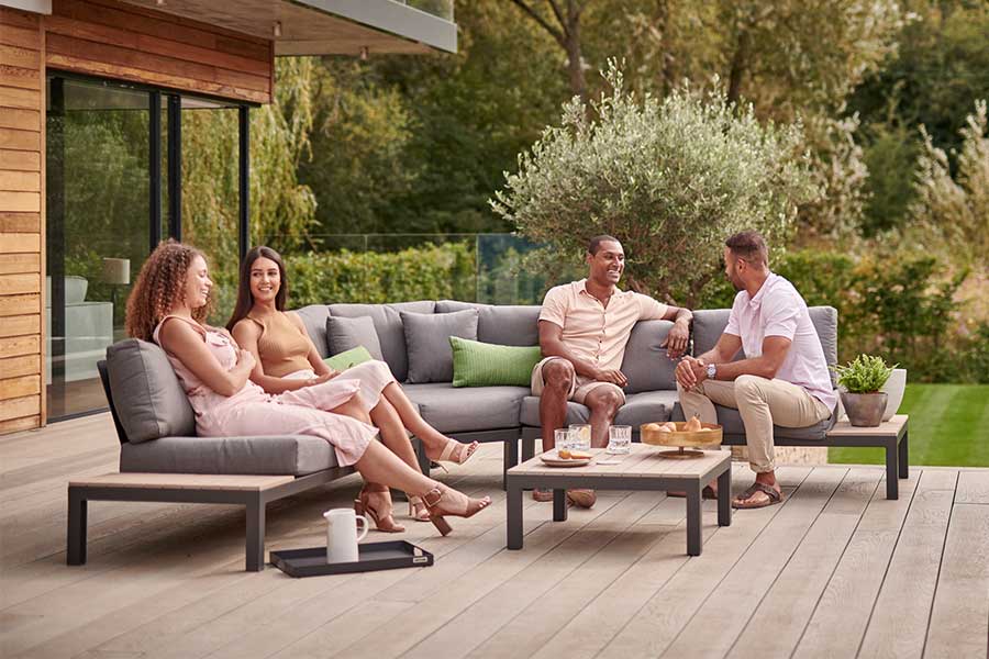Friends enjoying drinks in a sunny garden on metal corner lounge furniture 